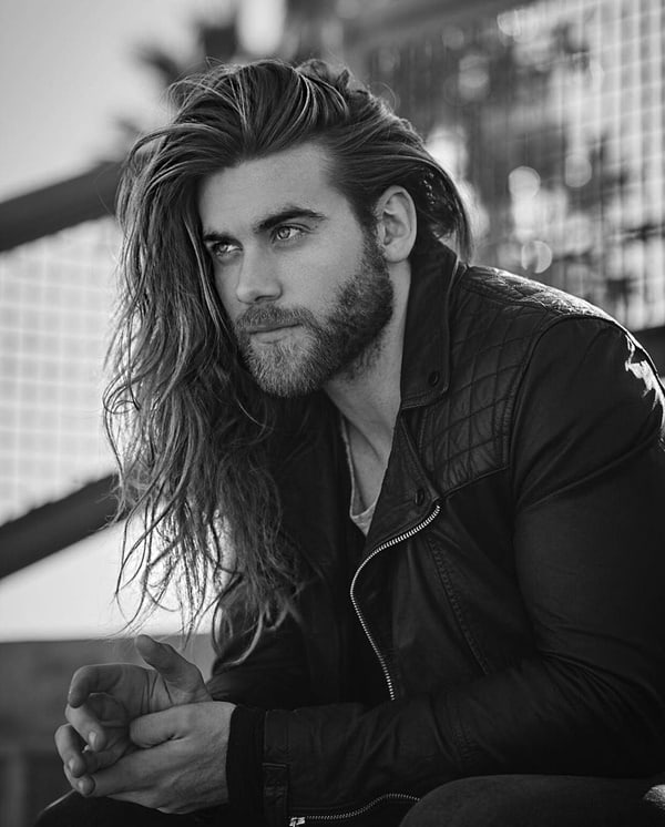 Close up image of fashionable young Caucasian man with long hair and ginger  beard posing outdoors wearing earring and facial piercing, having serious  look, squinting eyes because of sunshine foto de Stock |